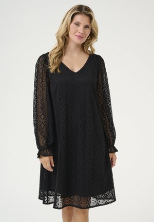 Black lace dress with a V-neck, long semi-sheer sleeves, and geometric patterns. Features a flared silhouette and ruffled cuffs.
