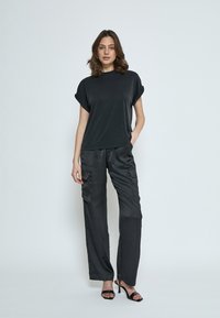 Top nera a maniche corte con una vestibilità rilassata abbinato a pantaloni cargo neri in satin con tasche laterali e una texture liscia.