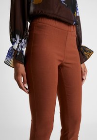 Pantalons extensibles marron au toucher lisse, dotés d'une taille élastique et d'une coupe ajustée qui épouse la jambe.