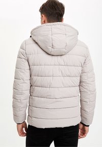 Světlá béžová prošívaná péřová bunda s kapucí, s žebrovanými detaily a černými akcenty na manžetách. Hladká, voděodolná tkanina.