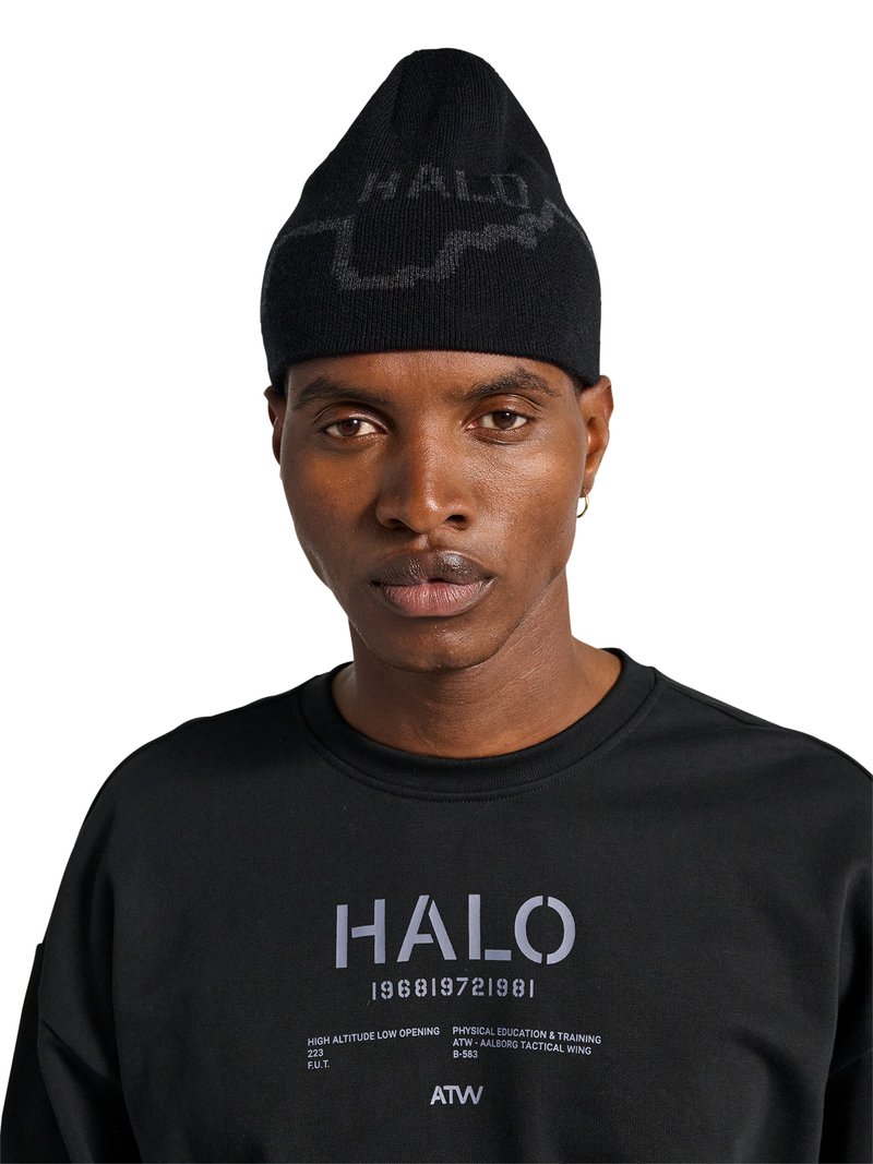 Man draagt een zwarte beanie met halftone tekst en een zwarte sweatshirt met de tekst “HALO 196819721981” en extra kleine tekst op de borst.
