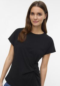 Camiseta negra de tela suave que presenta mangas cortas dobladas y un detalle de nudo torcido en la cintura para un ajuste relajado.