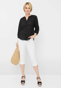 Camicia nera a maniche lunghe con bottoni e motivo testurizzato, abbinata a pantaloni capri bianchi, completata da una borsa in paglia intrecciata e sandali neri.
