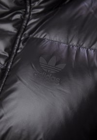 Black puffer jacket with a glossy texture, featuring a subtle embossed Adidas logo on the chest and stitched detailing.