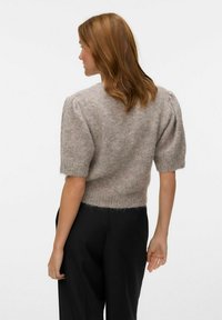 Maglione corto a maniche corte realizzato in morbido materiale peloso di colore beige chiaro. Caratterizzato da maniche a palloncino e vita aderente.