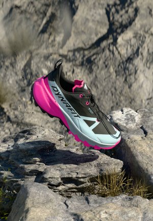 Black and turquoise trail running shoe with a pink sole, textured upper, and prominent laces; designed for outdoor stability and traction.