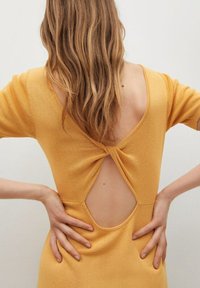 Robe en tricot jaune avec un décolleté en V et un détail de dos twisté, révélant la peau. Tissu texturé, manches longueur genoux et silhouette ajustée.