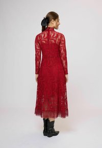 Červené čipkované šaty s dlhými rukávmi, vysokým golierom a priehľadnou látkou, zdobené zložitými kvetinovými vzormi a polopriesvitnou sukňou. V zadnej časti viditeľné gombíky.