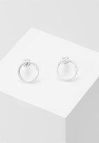 Silver circular stud earrings with a textured finish, mounted on a white pedestal. Simple and minimalist design.