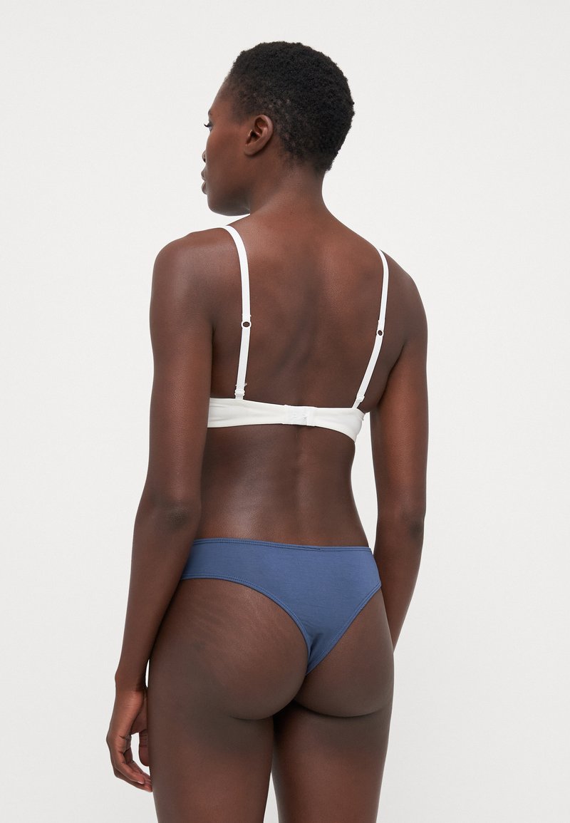 Bralette bianco con spalline regolabili e chiusura a gancio, abbinato a slip da bikini a vita bassa blu, tessuto morbido, design minimal.