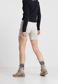 Ljusgrå shorts med en slät textur, kombinerade med beige vandringsskor och grå mönstrade strumpor, sedd bakifrån.