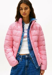 Lyserød pufferjakke med quiltet design og høj krave, lagdelt over en denimskjorte. Blå denimnederdel fuldender outfittet.