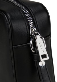 Angolo di una borsa in pelle nera con una cerniera metallica argentata e un tirazip. La superficie presenta una finitura testurizzata, evidenziando linee pulite e dettagli hardware.