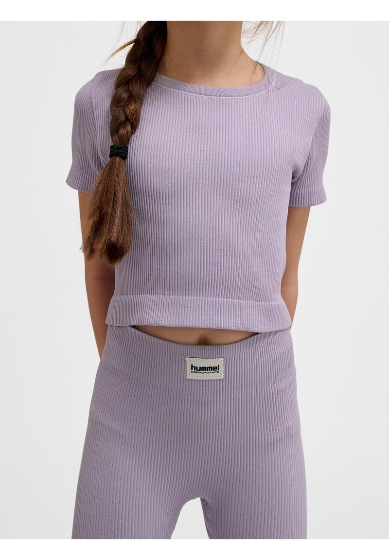 Jeune personne avec une longue tresse portant un haut court côtelé lavande assorti et des leggings taille haute avec une étiquette de marque à la taille.