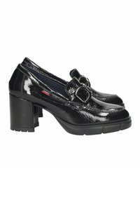 Zapatos de charol negro con tacón, con punta cuadrada, que presentan una correa prominente y un detalle de hebilla. Diseño de tacón ancho.