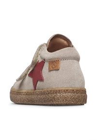 Chaussure en suède beige avec un accent en étoile rouge, semelle en caoutchouc texturé et patch en cuir beige. Présente un design à découpe basse et un talon plat.