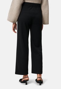 Czarne spodnie o szerokich nogawkach z gładkiego materiału i wysokim pasem. Posiadają podwójne tylne kieszenie, zestawione z czarnymi sandałami na obcasie z paskami.