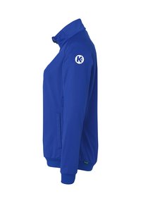 Blå lynlåsjakke med høj krave. Har sidelommer og et rundt logo på venstre ærme. Fremstillet af et glat, let stof.