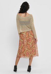 Une femme aux cheveux bouclés porte un pull léger et décontracté sur une jupe maxi colorée à motifs, accompagnée de bottines à talons noirs.