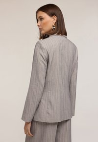Blazer grigio a righe con vestibilità sartoriale, colletto a coppetta e maniche lunghe. Presenta un tessuto liscio e dettagli di rifinitura puliti.