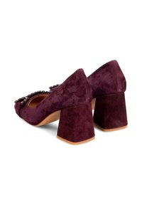 Zapatos de ante morado con tacón ancho y cuadrado, punta redondeada y detalle decorativo de cuentas en la parte delantera. Superficie texturizada y construcción sólida.