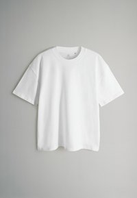 Biała bawełniana koszulka z krótkim rękawem, okrągłym dekoltem i luźnym krojem. Gładka tekstura, prosty dół i brak widocznych wzorów lub akcentów.