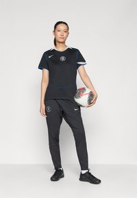 Svarte fotballtrøye med blå detaljer, shorts og svarte fotballsko. Mønstret fotball holdes i den ene hånden. Har Nike-logo og klubbemblem.