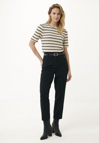 Maglione a maglia con motivo zigzag nero e crema, abbinato a pantaloni neri a vita alta e stivaletti, con una fibbia circolare in vita.