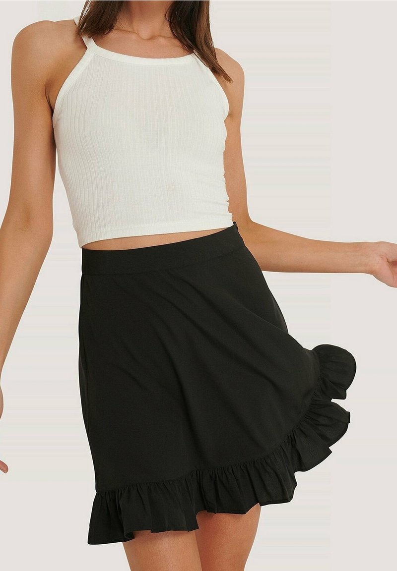Top corto bianco a costine con spalline sottili abbinato a una mini gonna nera a balze. La gonna presenta una silhouette svasata e un tessuto strutturato.