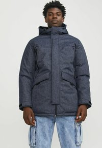 Chaqueta acolchada de color azul marino con un alto cuello y capucha, que cuenta con dos bolsillos frontales y cierre de cremallera, hecha de un tejido texturizado y resistente al agua.