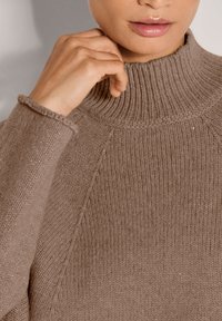 Strickpullover in hellem Braun mit einem hohen Rippenkragen, strukturiertem Muster und enganliegendem Schnitt. Mit sichtbaren Nähten entlang der Nähte.