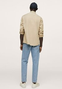 Chemise kaki à manches longues avec col à boutons, associée à un jean en denim bleu clair et des baskets blanches. Design minimaliste, coupe décontractée.