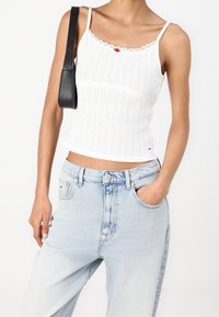 Vitt ribbat linne med spetsdetaljer och röd accent, parat med ljusblå högmidjade jeans med en klassisk fickdesign.