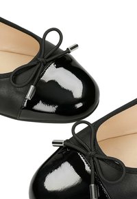 Zwarte ballerina's met een glanzende neus, een leren body met textuur, een zwart strikdetail en zilveren accenten. Ronde vorm en een gladde afwerking.