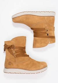 Tan suède enkellaarzen met elastische banden, ronde neus en een gevoerde zool. Beschikt over een logo aan de zijkant en een gestrikte accent achteraan.