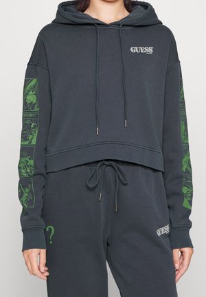 Sweat à capuche court gris foncé et pantalon de survêtement avec des motifs de bande dessinée verts sur les manches et un point d'interrogation vert sur la jambe gauche.