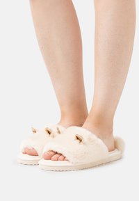 Faux fur slide slippers in off-white with open toe. Features gold-tone hardware and plush texture, mounted on a durable white sole.