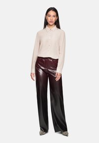 Beige button-up blouse with long sleeves, paired with high-waisted burgundy faux leather pants. Features a relaxed fit and a smooth texture.