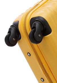 Valigia rigida gialla con superficie texturizzata, ruote nere e chiusura a zip. Presenta bordi arrotondati e hardware resistente.