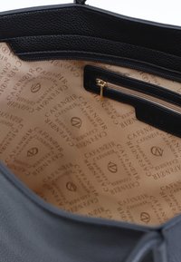 Svart läderhandväska med insida som har en slät, ljusbrun foder med upprepade logotyper. Innehåller en dragkedjeficka och svarta accenter.