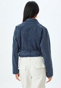 Marinrandig kort jacka med krage, som har ett knytbälte och långa ärmar. Tyget är slätt med en subtil textur.