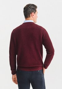 Bordowy sweter z ryżowym splotem, z długimi rękawami, okrągłym dekoltem i mankietami, zestawiony z ciemnymi spodniami. Miękka tekstura i luźny krój.