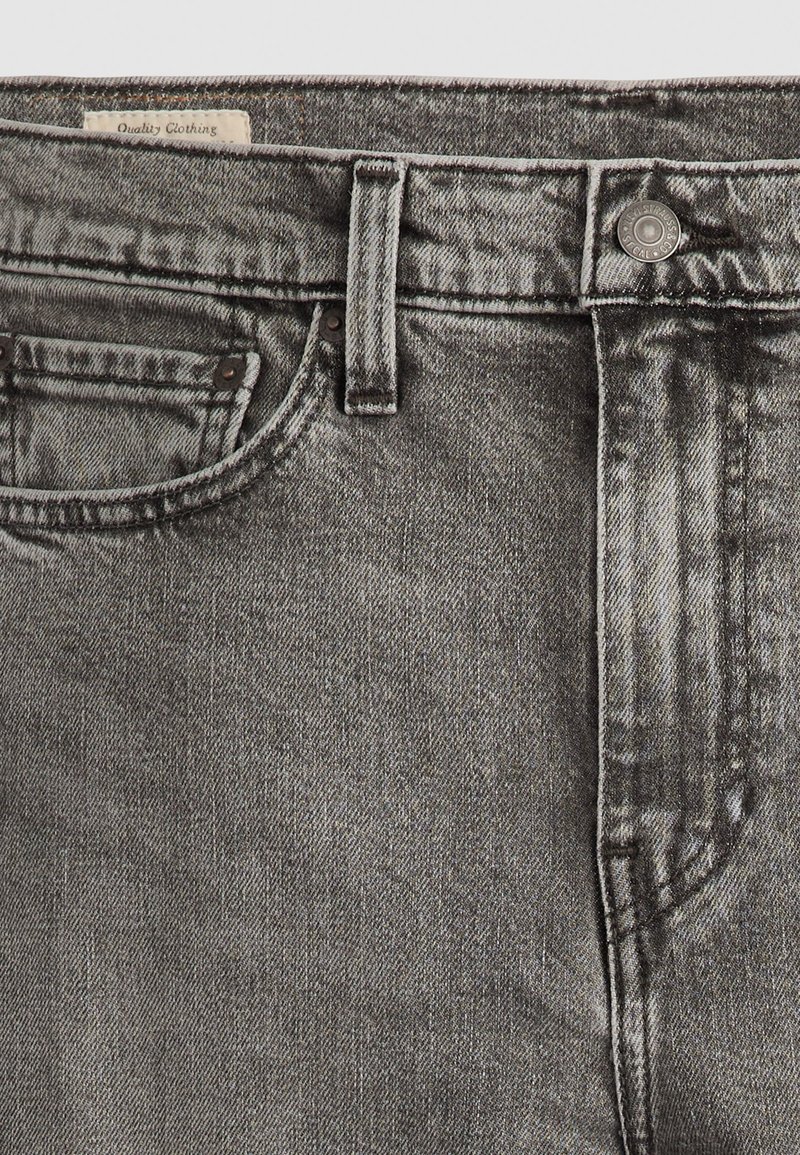 Jeans en denim gris avec une finition décolorée, fermeture à bouton et design classique à cinq poches, avec des coutures visibles et des détails de texture.