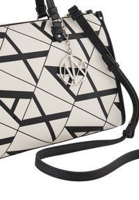 Borsa bianca con motivi geometrici neri. Superficie texturizzata, con un ciondolo logo argentato e tracolla nera. Forma rettangolare compatta.