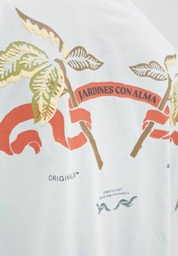 Witte katoenen t-shirt met kleurrijke botanische graphics, inclusief bladeren en een strik met de tekst "JARDINES CON ALMA". Lichtgewicht stof.