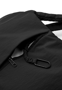 Bolsa de tela negra con superficie texturizada, que cuenta con un bolsillo con cremallera, cordón ajustable y un mosquetón negro.