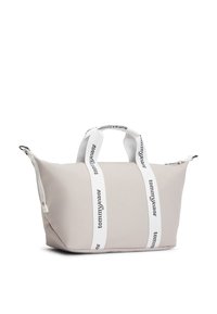 Μπεζ τσάντα ώμου από ανθεκτικό ύφασμα με λευκές λαβές που φέρουν εκτυπωμένο λογότυπο "tommy jeans". Κλείσιμο με φερμουάρ και απαλή υφή.