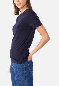 Marineblauwe katoenen T-shirt met korte mouwen en ronde hals, met een aansluitende pasvorm en subtiele logo-detailing aan de zoom, gecombineerd met denim jeans.