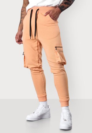 Pfirsichfarbene Cargo-Jogginghosen aus weichem Stoff mit schlanker Passform, elastischem Bund, schwarzen Kordeln und seitlichen Reißverschlusstaschen.