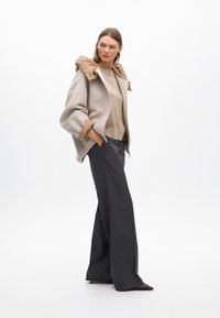 Bež jakna na zip s tamnosmešnim pufastim kapuljačom, uparena s svijetlobez krem majicom i tamnim hlačama širokih nogavica s prugama. Glatke teksture i čiste linije.